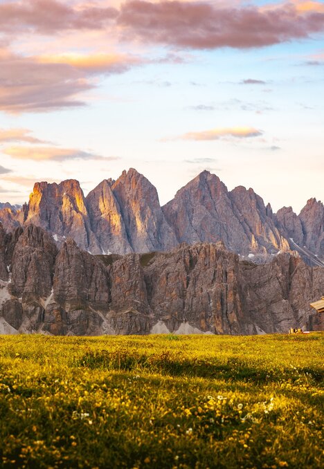 Almwiese mit kleiner Holzhütte und Dolomitengipfeln bei Sonnenaufgang. | © Matthias Gasser