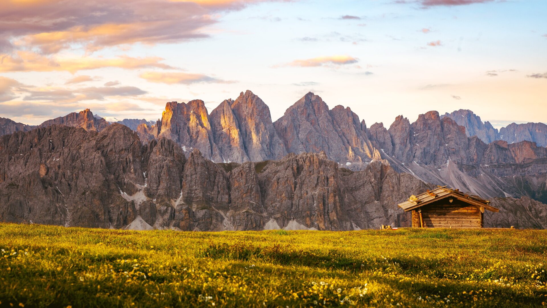 Mountain meadow with a small wooden hut and Dolomite peaks at sunrise. | © Matthias Gasser