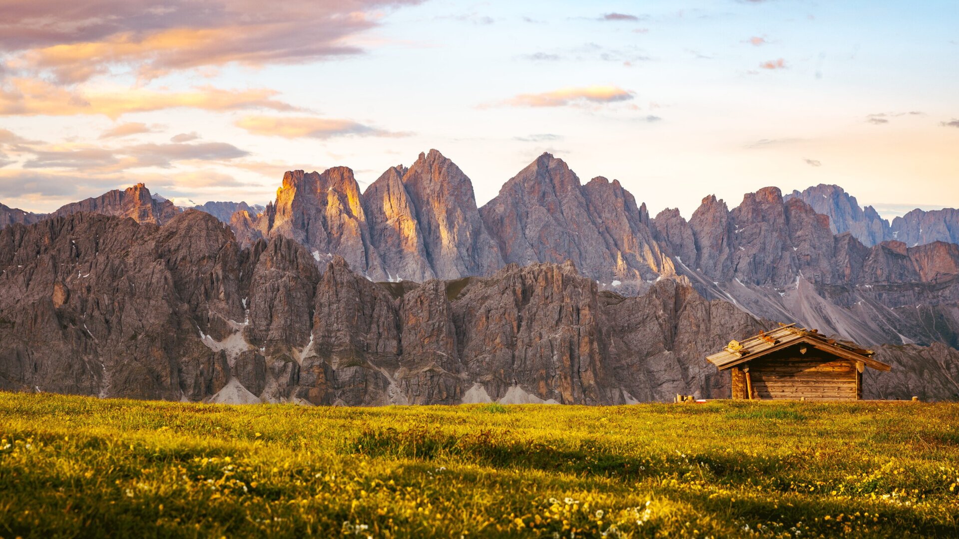 Almwiese mit kleiner Holzhütte und Dolomitengipfeln bei Sonnenaufgang. | © Matthias Gasser