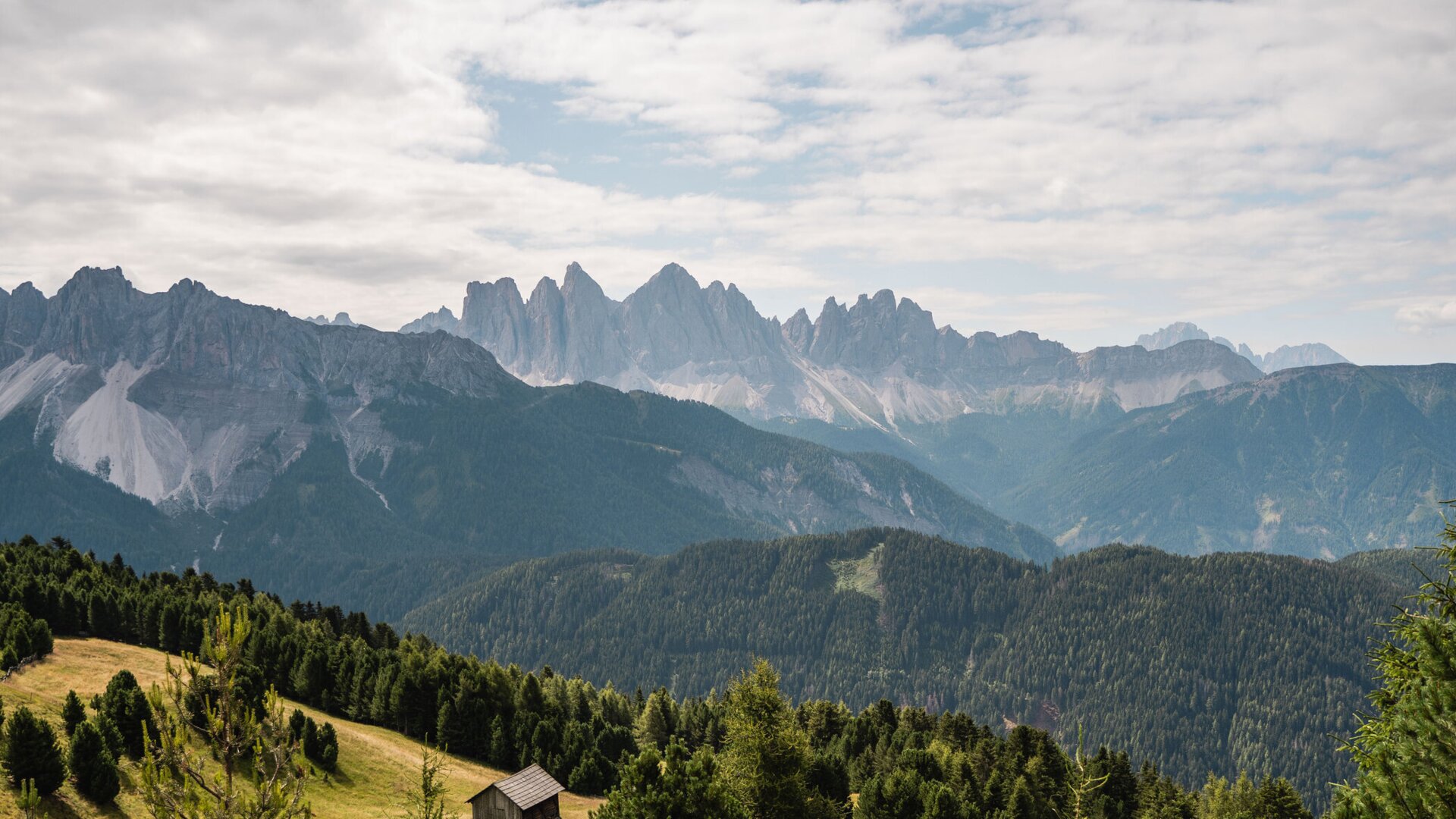 Panorama di montagna con colline boscose, una piccola baita e cielo nuvoloso. | © (c) Horeca