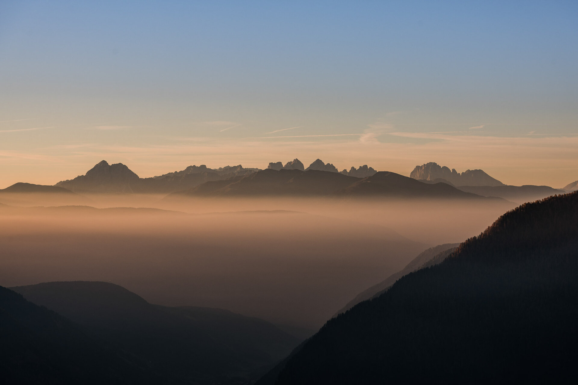 Cime di montagna sopra una valle nebbiosa all’alba con cielo blu e arancione. | © (c) Wisthaler