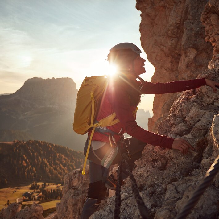 Arrampicatore su una parete rocciosa al tramonto con vista sulla valle in basso.