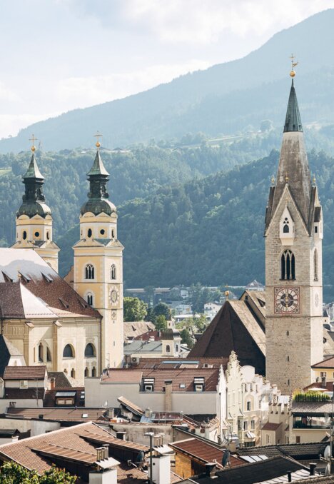 Church towers and rooftops in Brixen Südtirol with green mountains in the background. | © (c) Thomas Rötting