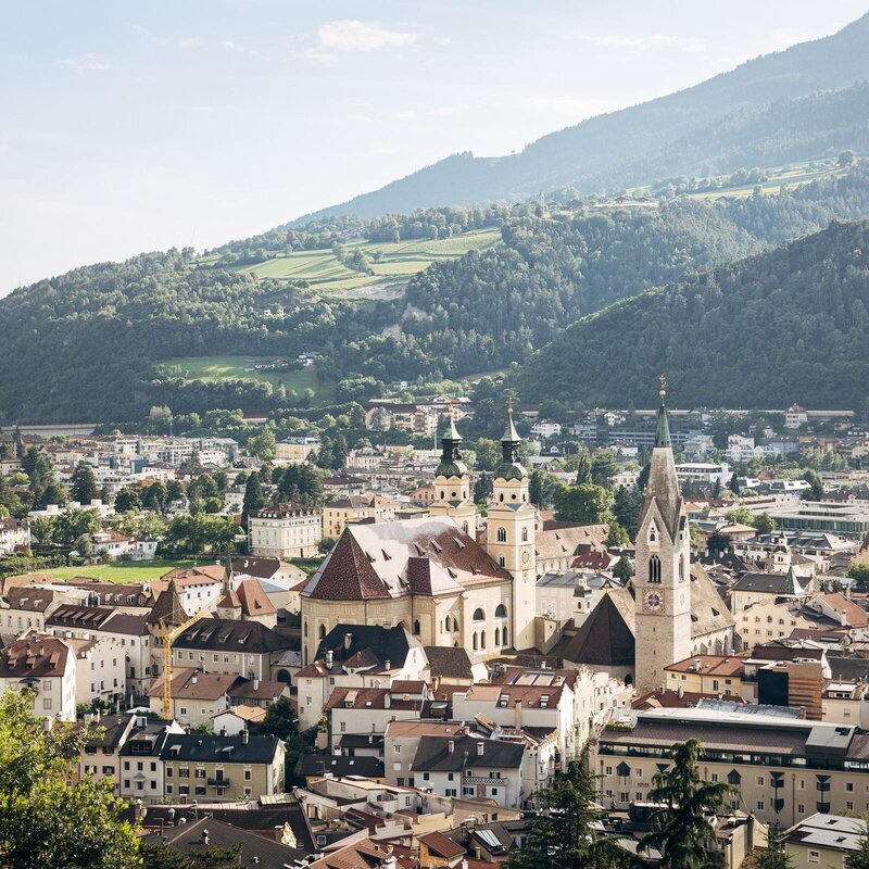 Vista su Brixen Südtirol con il centro storico, i campanili e i pendii verdi.