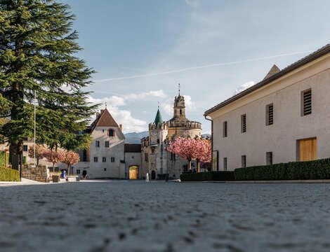Piazza storica con porta del castello, alberi e fioritura a Brixen Südtirol