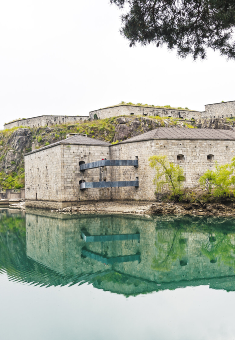 Forte in pietra riflesso nelle calme acque verdi ai piedi dei versanti montani
