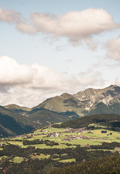 Grünes Alpentall mit verstreuten Dörfern und Berggipfeln unter bewölktem Himmel. | © (c) Hannes Niederkofler