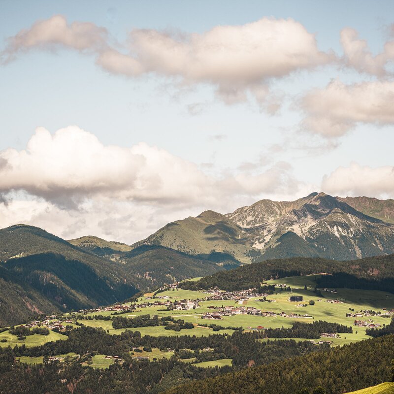 Valle alpina verde con piccoli villaggi e cime montuose sotto un cielo nuvoloso. | © (c) Hannes Niederkofler
