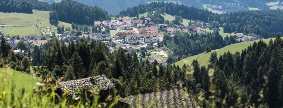 Vista su un paese di valle con chiesa, prati e colline boscose in estate.