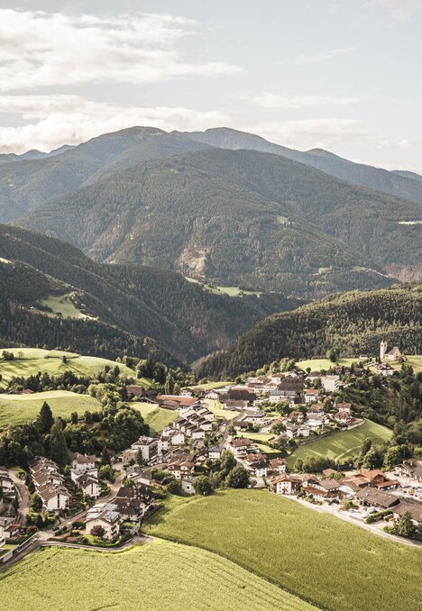 Ein Dorf in einem grünen Alpental mit Bergen im Hintergrund.