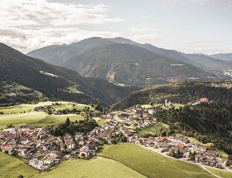 Ein Dorf in einem grünen Alpental mit Bergen im Hintergrund.