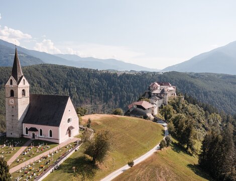 Chiesa su una collina con cimitero, ruderi di castello e montagne boscose sullo sfondo. | © Brandnamic
