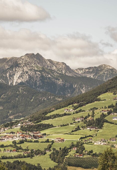 Green valley with a village beneath the mountains in Brixen Südtirol, under a cloudy sky. | © Hannes Niederkofler