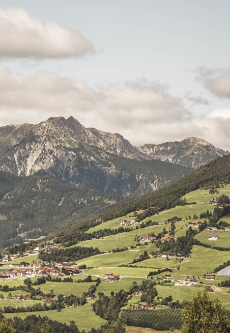 Green valley with a village beneath the mountains in Brixen Südtirol, under a cloudy sky.