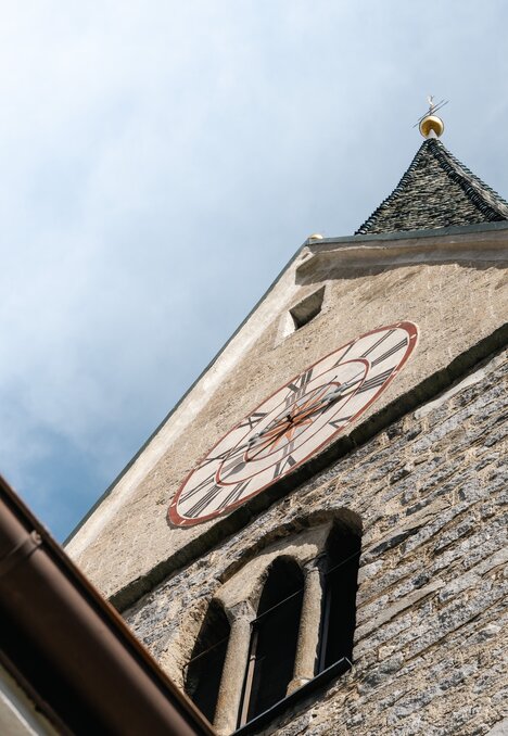 Campanile in pietra con orologio visto dal basso contro il cielo azzurro