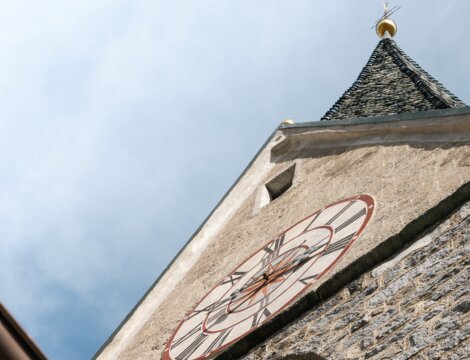 Steinerner Kirchturm mit Uhrzifferblatt von unten vor blauem Himmel