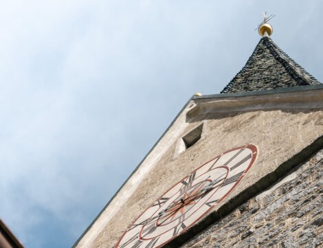 Steinerner Kirchturm mit Uhrzifferblatt von unten vor blauem Himmel