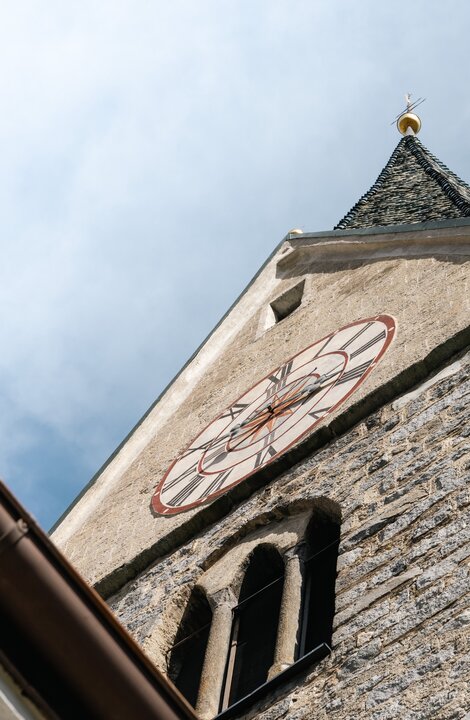 Steinerner Kirchturm mit Uhrzifferblatt von unten vor blauem Himmel
