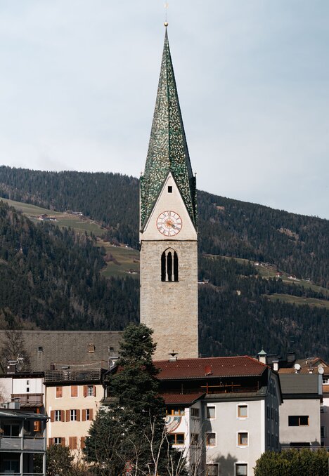 Kirchturm über einem Dorf mit verschneiten Bergen im Hintergrund in Brixen Südtirol.