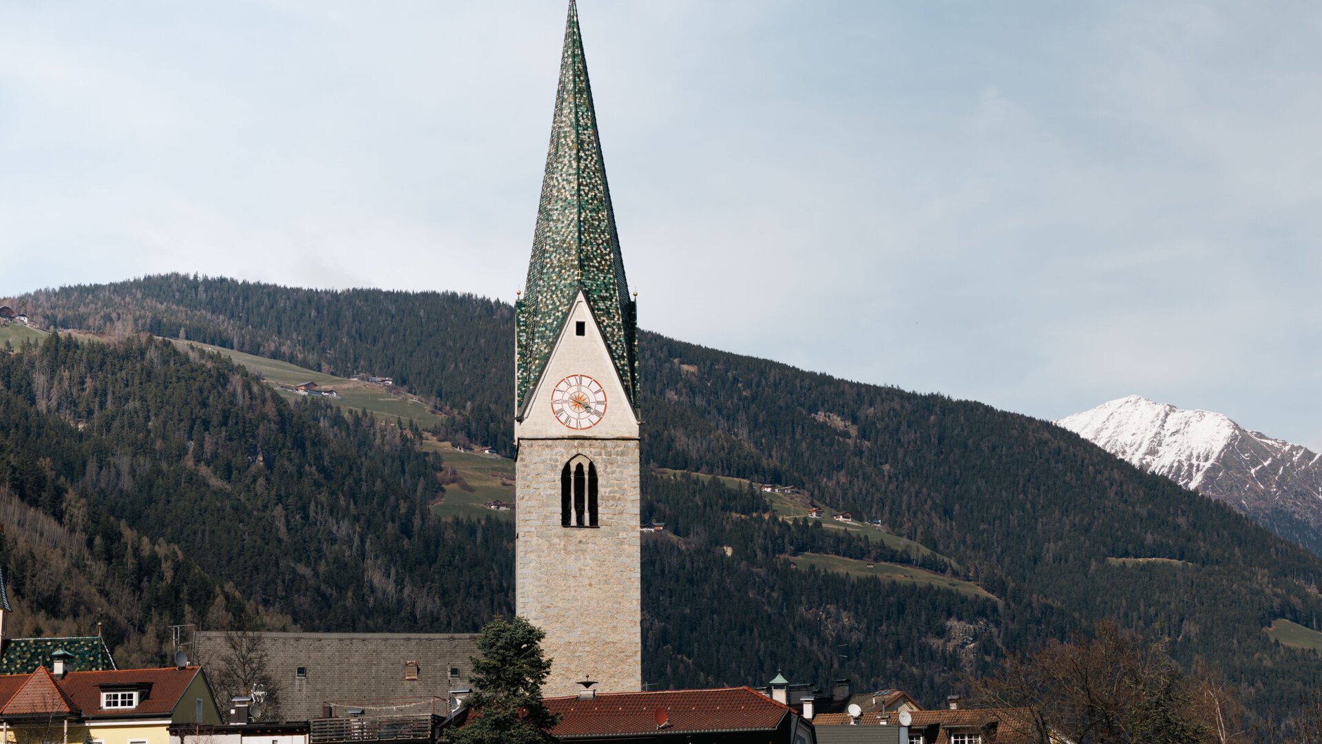 Church tower above a village with snowy mountains in the background in Brixen Südtirol.