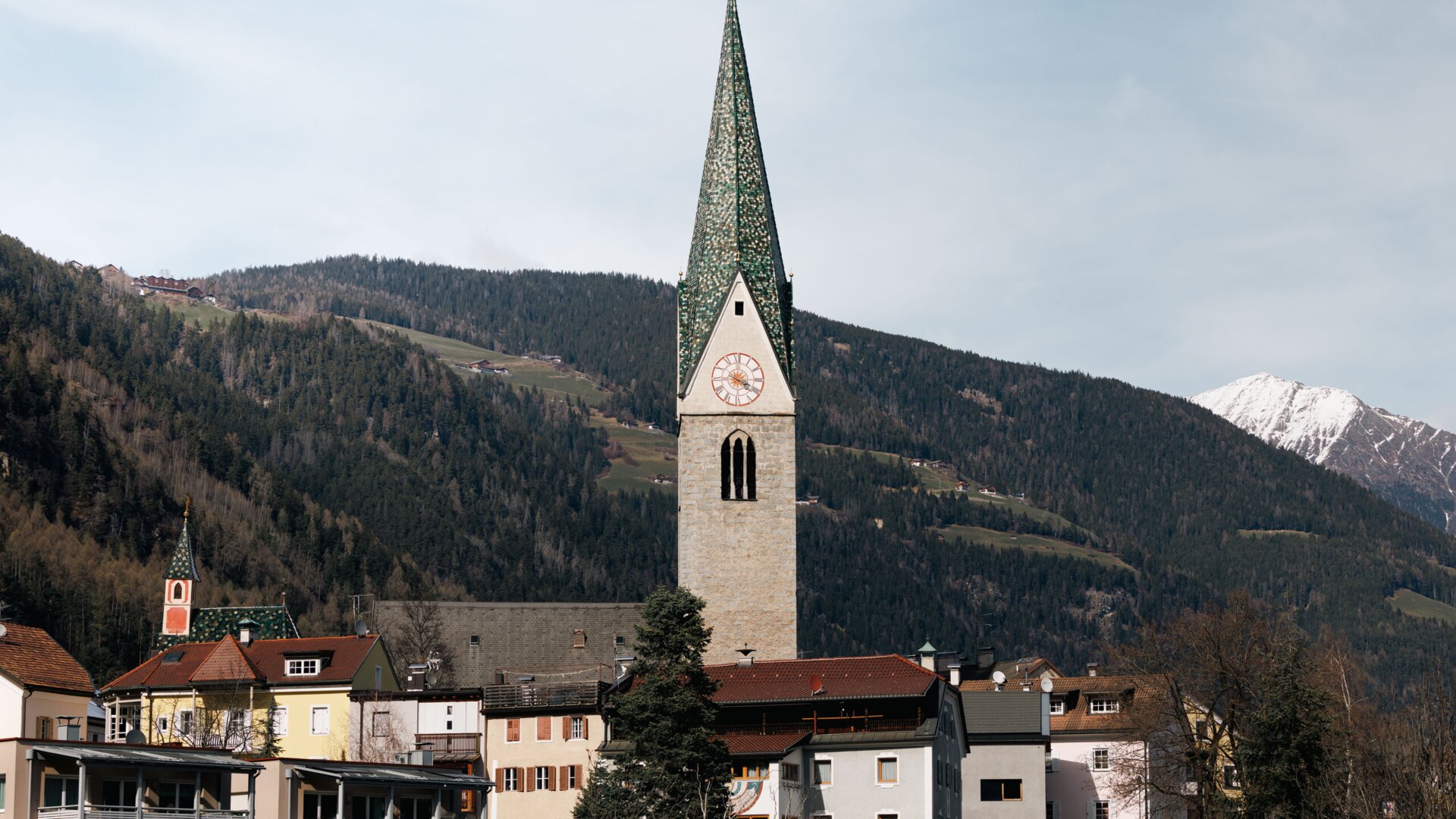 Church tower above a village with snowy mountains in the background in Brixen Südtirol.