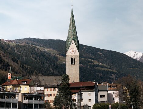 Kirchturm über einem Dorf mit verschneiten Bergen im Hintergrund in Brixen Südtirol.