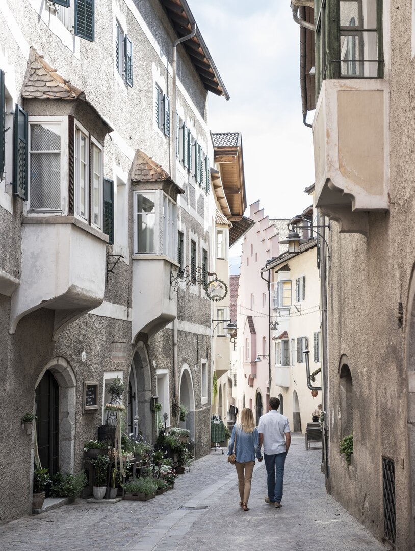 Una coppia cammina in un vicolo storico stretto di Brixen Südtirol con facciate antiche e portici.