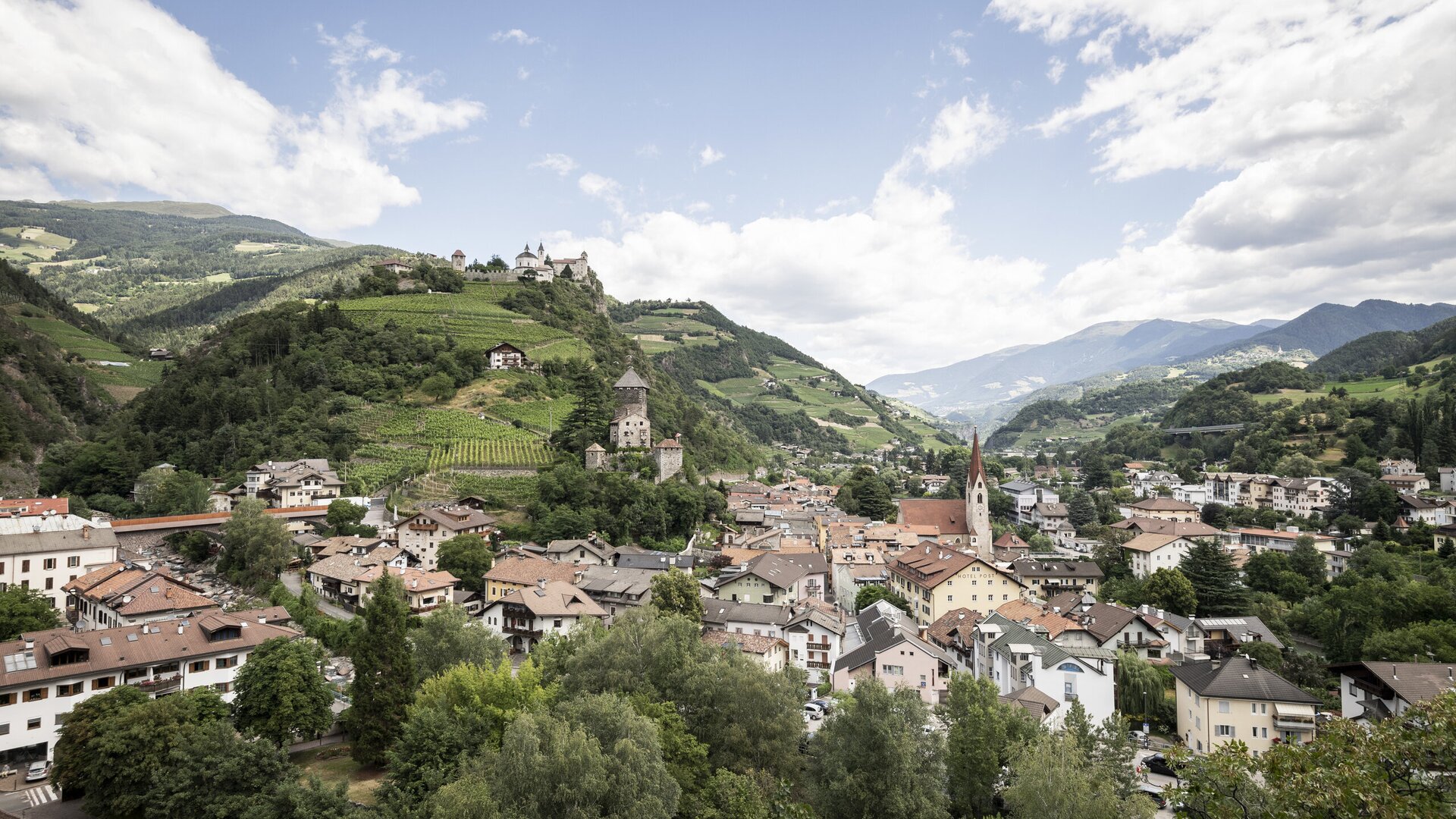 Panoramic view over Brixen Südtirol with church towers, hillside homes and green mountains under cloudy sky