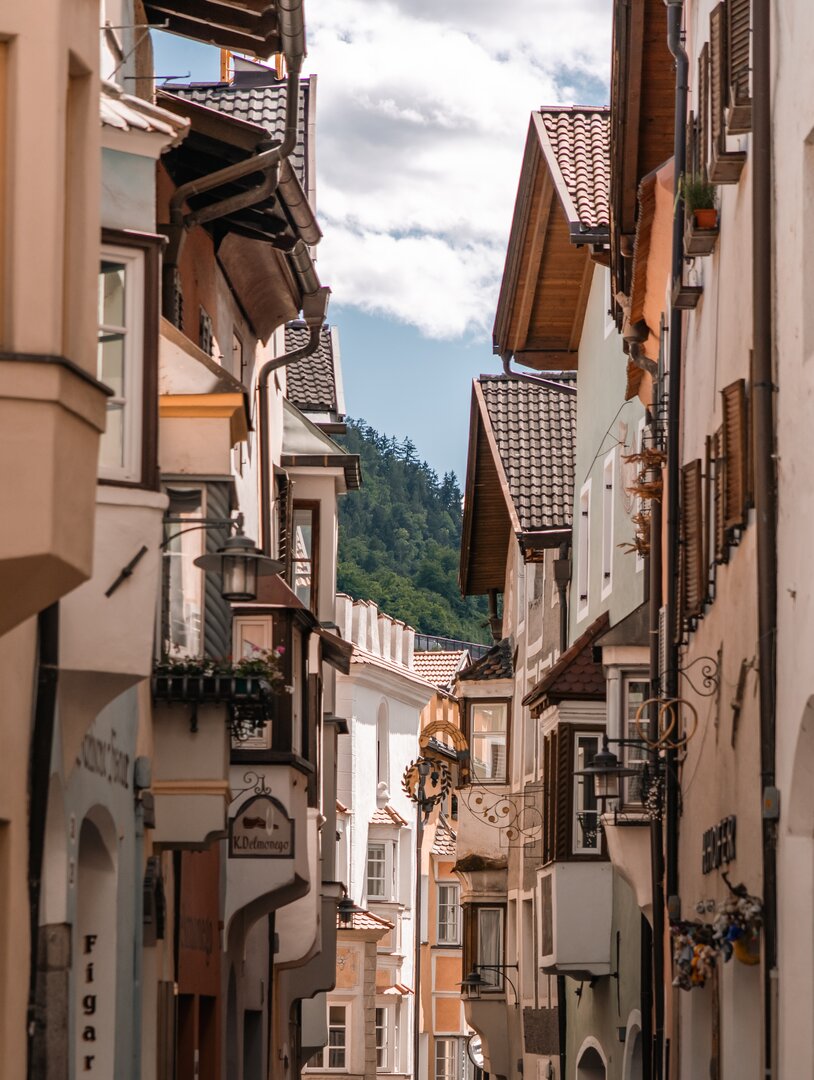 Historic alley in the old town of Klausen with traditional house façades and a view of the wooded hillside. | © Brixen Südtirol Dolomites Italy