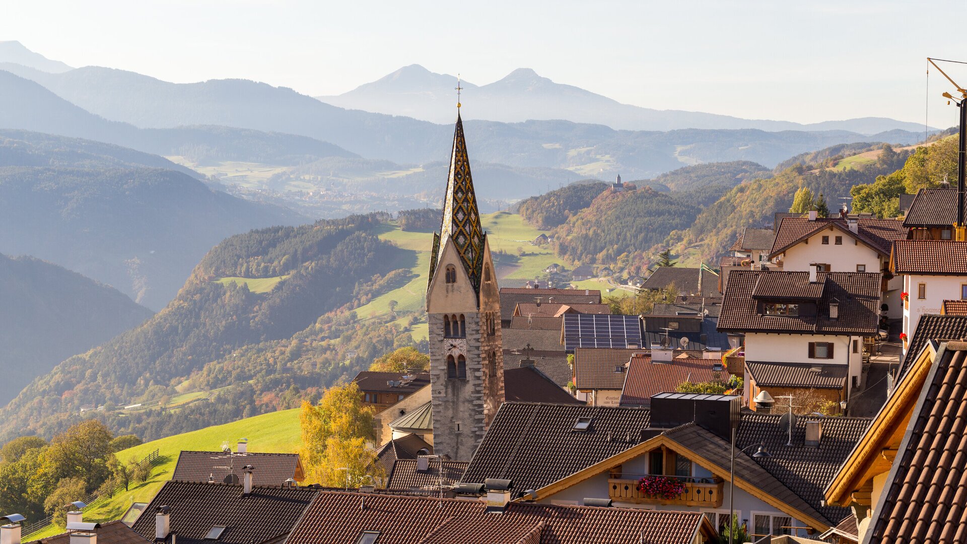 Village with church steeple above a green valley and Alpine mountains