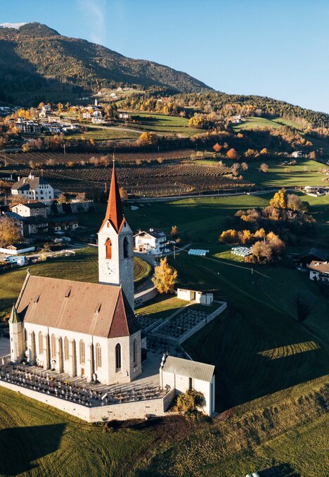 Kirche über einem Dorf in einem grünen Bergtal im warmen Herbstlicht.