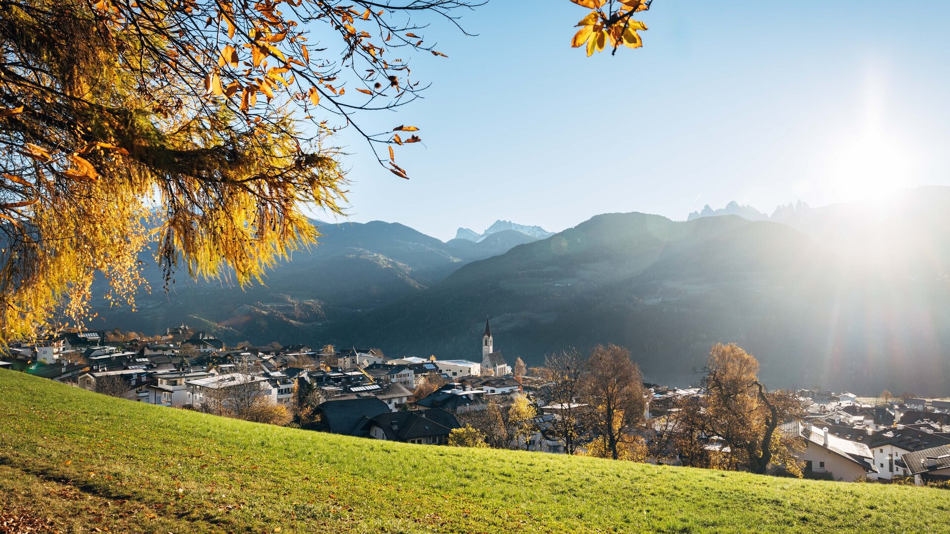 Autumn view over Brixen Südtirol with a village in the valley, mountains and sunlit trees.