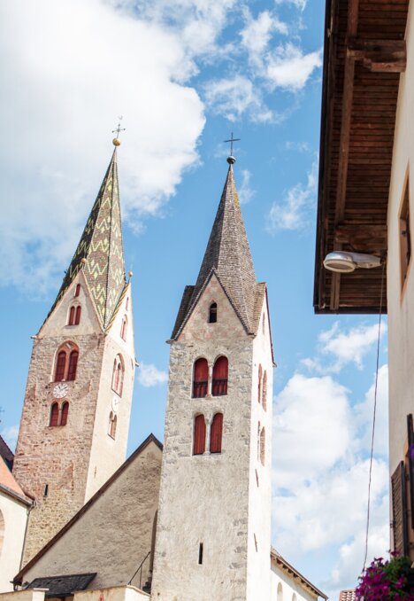 Kirchtürme und eine blumengeschmückte Hausfassade unter blauem Himmel in Brixen Südtirol.