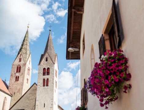 Church towers and a flowered house facade under a blue sky in Brixen Südtirol.