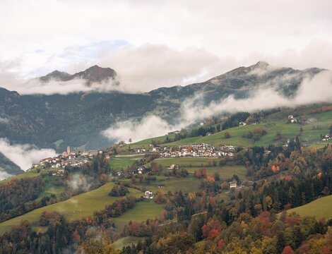 Bergdorf mit Nebel über grünen Almhängen im Herbst