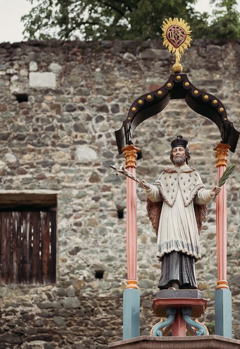 Statua di un santo sotto un baldacchino decorato accanto a un antico muro in pietra a Brixen Südtirol.