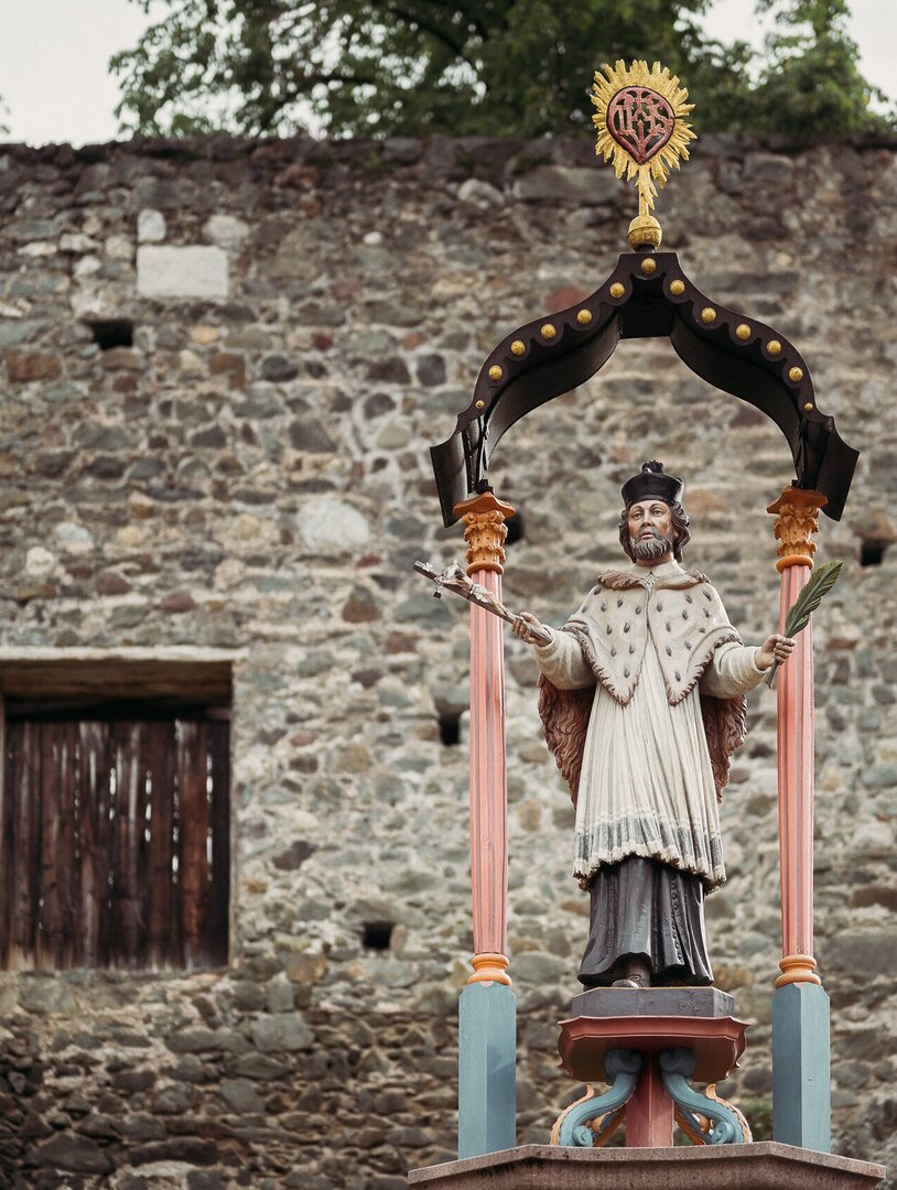 Statua di un santo sotto un baldacchino decorato accanto a un antico muro in pietra a Brixen Südtirol.