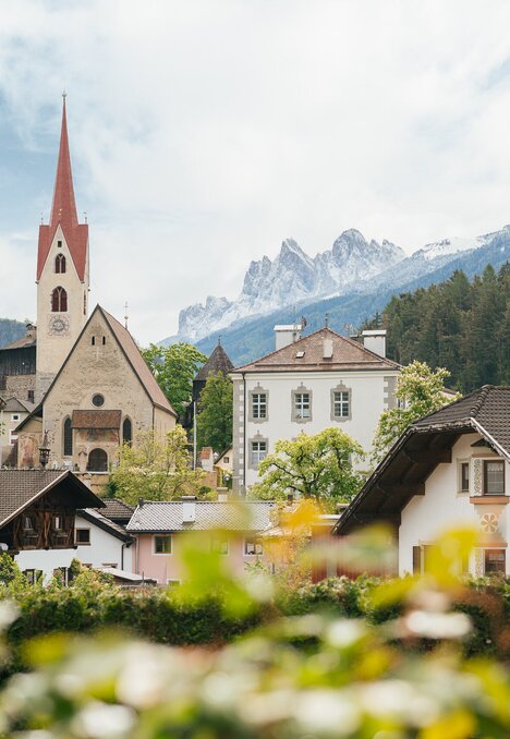 Chiesa di paese con campanile rosso a Brixen Südtirol, tra case alpine e cime montane.