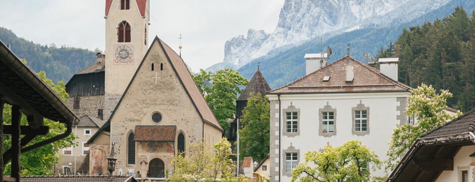 Chiesa di paese con campanile rosso a Brixen Südtirol, tra case alpine e cime montane.