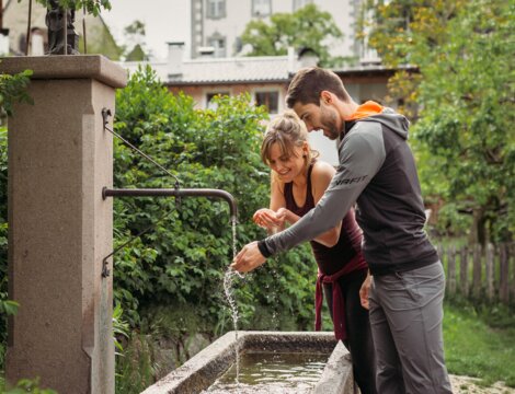 Coppia che riempie l'acqua a una fontana di paese a Brixen Südtirol.