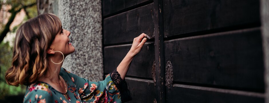 Donna che apre una porta di legno scuro accanto a un muro in pietra all’aperto.