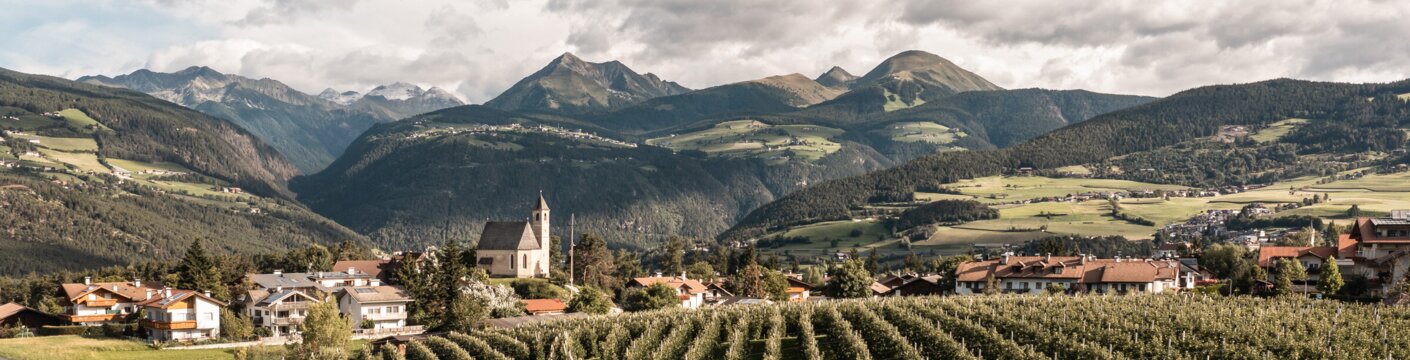 Vineyards below a village and church in a valley with mountain views in Brixen Südtirol
