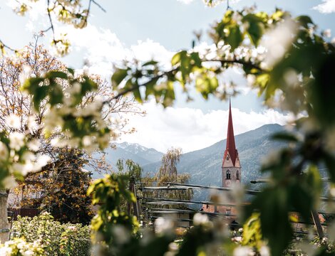Kirchturm, eingerahmt von Frühlingslaub, mit Bergen im Hintergrund in Brixen Südtirol.