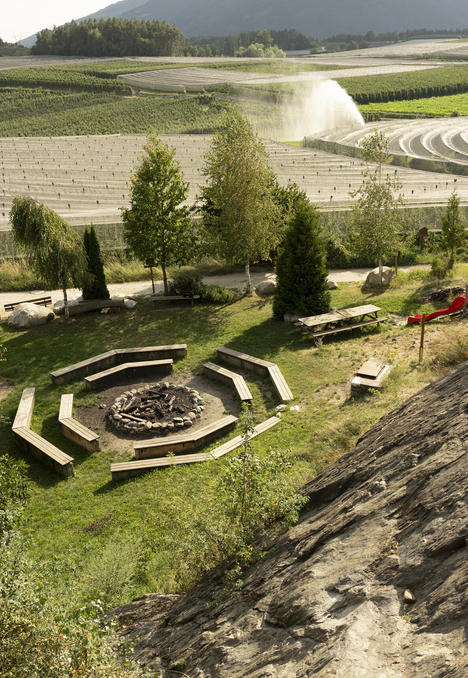 A grassy hillside with a fire pit and benches overlooking fields and mountains.