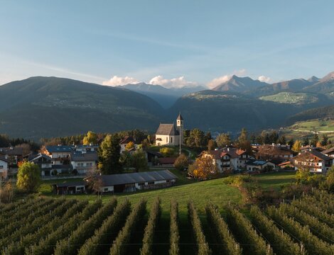 Village with church, green fields and vineyards below the mountains