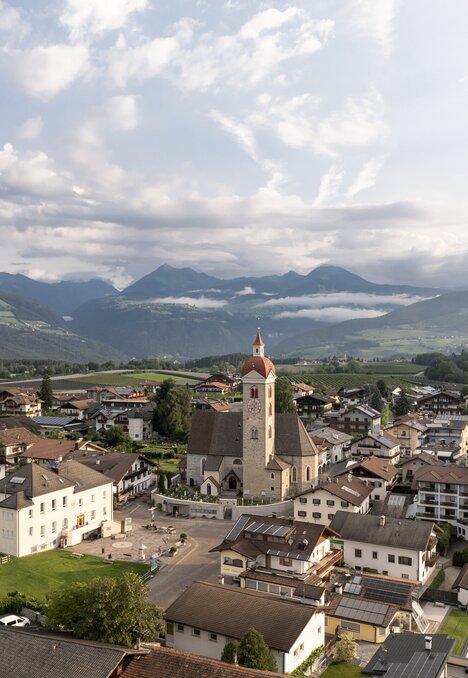 Aerial view of Brixen Südtirol with a church, town houses and mountain valley under cloudy sky.