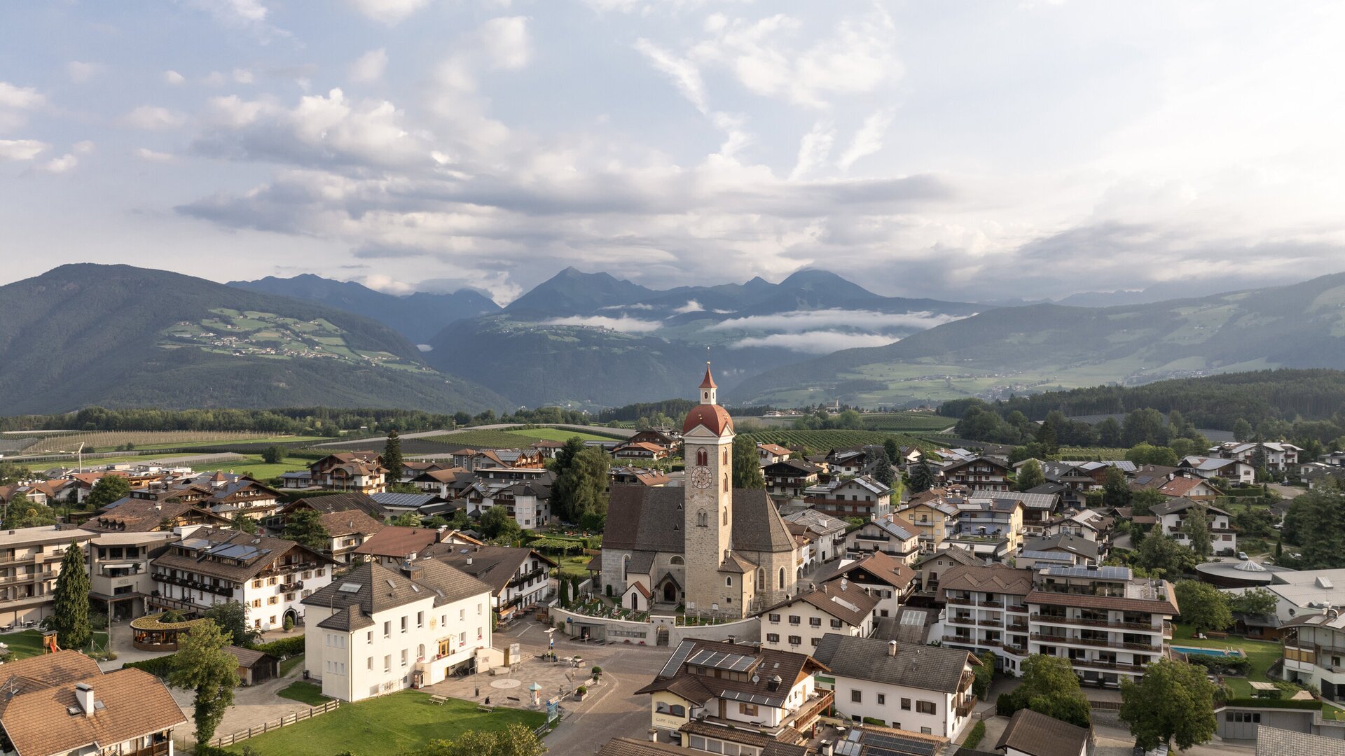 Aerial view of Brixen Südtirol with a church, town houses and mountain valley under cloudy sky.