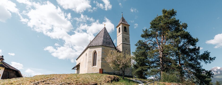 Small hilltop church with a path, trees and blue sky in the Alps