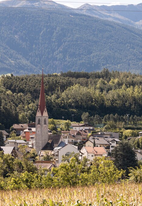Sunny village with a church spire, forest and mountain backdrop in Brixen Südtirol.
