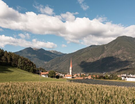Paese con campanile nella valle di Brixen Südtirol, circondato da montagne e campi